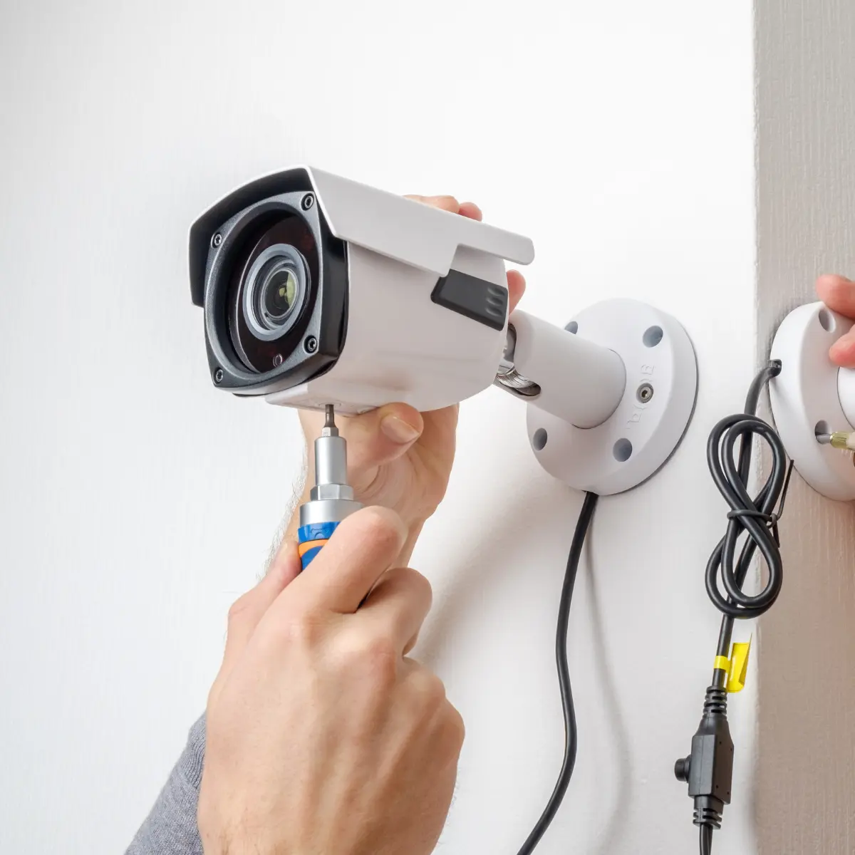 Technician screwing a white bullet CCTV camera onto a wall bracket