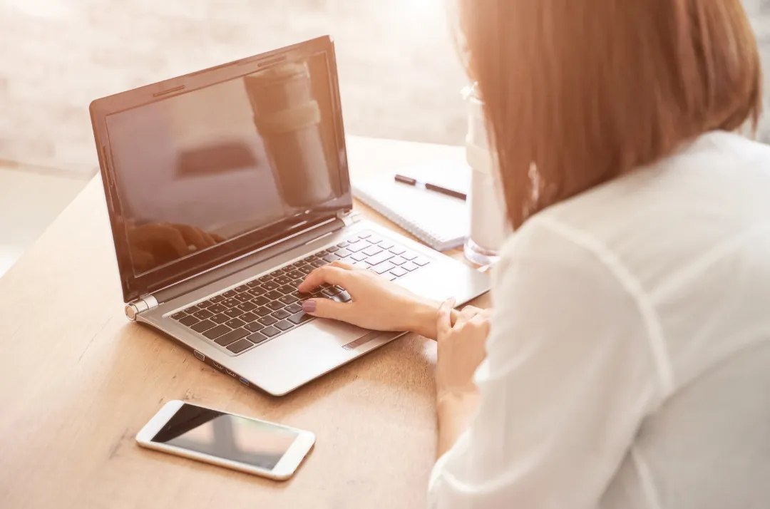 Person working on a laptop at a wooden desk with a phone beside it