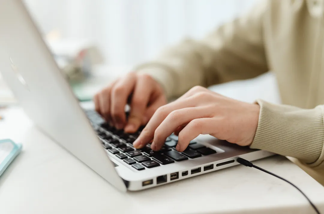 Hands typing on a laptop at an office desk